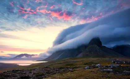 Sunset over Snæfellsnes Peninsula with dramatic clouds rolling over the mountains, creating a picturesque Icelandic landscape.