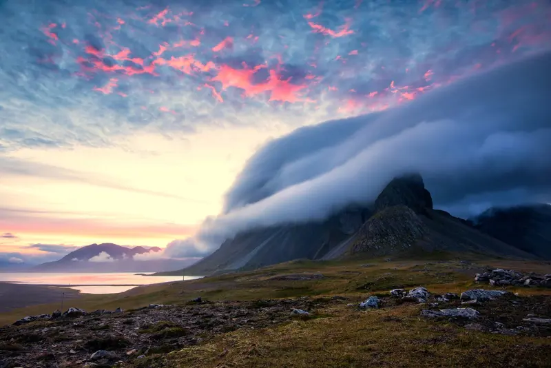 Sunset over Snæfellsnes Peninsula with dramatic clouds rolling over the mountains, creating a picturesque Icelandic landscape.
