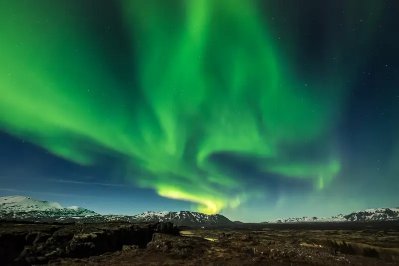 Northern lights at Þingvellir National Park reaching over mountain range in the background.