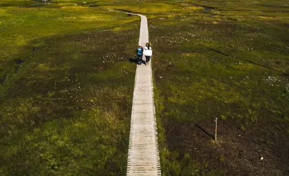 A wooden boardwalk leading through a moss-covered valley toward Landmannalaugar's geothermal area.