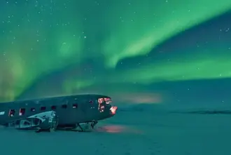 Solheimafjara Black Sand Beach completely snow covered with the airplane wreck sitting under the Northern Lights in Iceland.