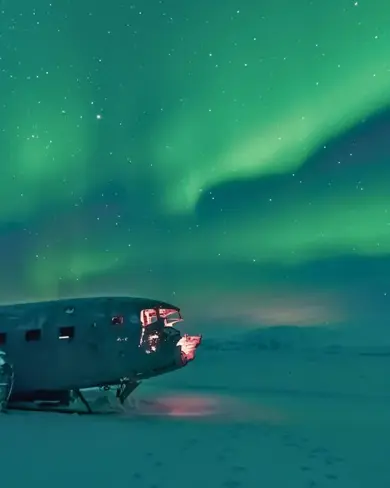 Solheimafjara Black Sand Beach completely snow covered with the airplane wreck sitting under the Northern Lights in Iceland.