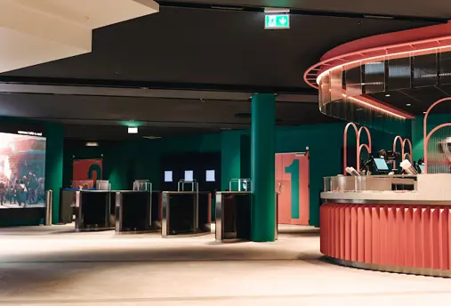 Interior view of Sambíóin Kringlan cinema in Reykjavík, featuring modern design with green walls, pink counters, and ticket gates, offering a stylish movie-going experience.