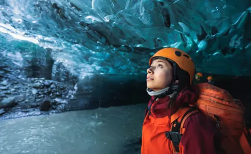 Adventurous female traveler exploring Vatnajökull’s crystal blue ice cave in Iceland wearing a helmet and winter gear.