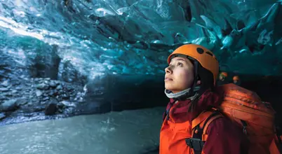 Adventurous female traveler exploring Vatnajökull’s crystal blue ice cave in Iceland wearing a helmet and winter gear.