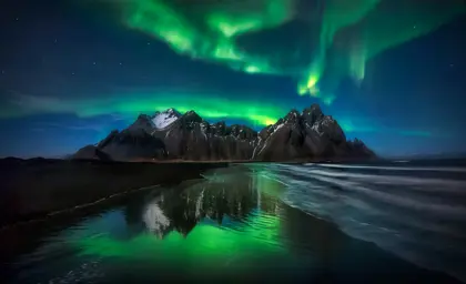 Northern Lights shining brightly over Vestrahorn mountain in Iceland, featured as a banner for Travel Reykjavik's tour promotions.