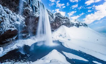 Frozen Seljalandsfoss waterfall in Iceland framed by thick snow and ice on a bright winter day.