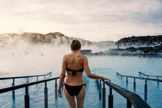 Woman enjoying a serene morning dip in the steamy waters of the Blue Lagoon geothermal spa in Iceland at sunrise.