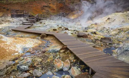 A steamy geothermal area with wooden pathways winding through Seltún in Krýsuvík, Iceland, showcasing the vibrant colors of the mineral-rich landscape. Perfect for nature exploration and photography.