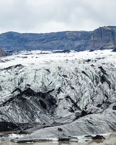 Close-up of Sólheimajökull Glacier in Iceland, featuring a rugged mix of white ice and black volcanic ash under cloudy skies, showcasing the glacier's dramatic landscape.