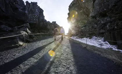 Visitors walking along the Thingvellir National Park pathway with sunlight peeking through the cliffs