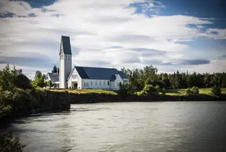 The historic Selfoss church with its tall steeple standing by a peaceful river in Selfoss, Iceland.