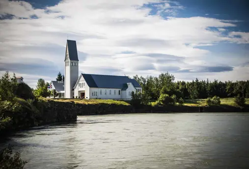 The historic Selfoss church with its tall steeple standing by a peaceful river in Selfoss, Iceland.