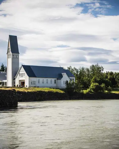 The historic Selfoss church with its tall steeple standing by a peaceful river in Selfoss, Iceland.