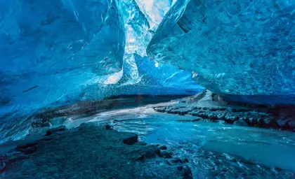 Serene scene of an underground river flowing through a vibrant blue ice cave in Iceland, captured during a Travel Reykjavik glacier tour experience.