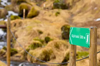Green trail sign pointing 300 meters toward Gljúfrabúi Waterfall, surrounded by Icelandic countryside.