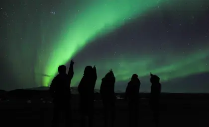 A group of people silhouetted against the night sky, watching the Northern Lights during an Icelandic tour, showcasing the breathtaking natural phenomenon in a dark starry sky.