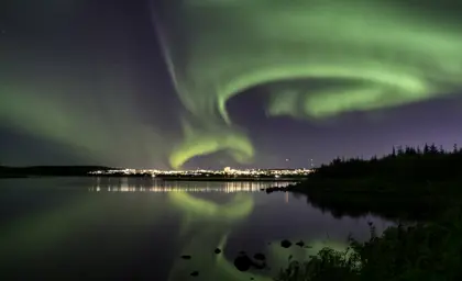 Mesmerizing view of the Northern Lights dancing over Reykjavik, reflecting in the serene waters of a lagoon at night.
