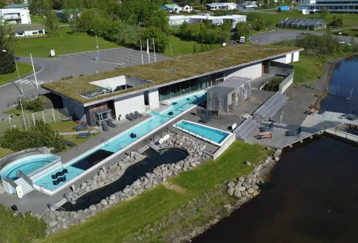 Aerial view of Fontana geothermal spa in Iceland, with outdoor pools surrounded by greenery and modern architecture, offering a unique relaxation experience.