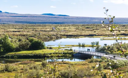 Scenic view of Þingvellir National Park with a bridge crossing over reflective waters and distant volcanic landscapes, captured on a sunny day during the Journey Around Iceland tour by Travel Reykjavik.