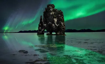 The stunning Hvitserkur rock formation under the Northern Lights, reflecting on the calm waters in Iceland.