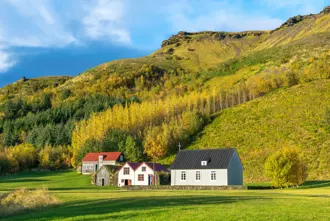 Skógar folk museum in Iceland with turf farm and church bathed in sunlight under green hills.