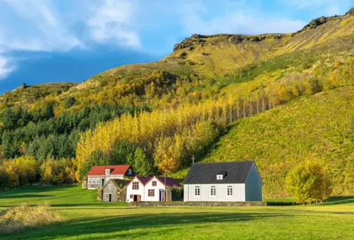 Skógar folk museum in Iceland with turf farm and church bathed in sunlight under green hills.
