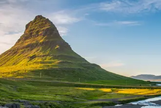 Scenic view of the Snæfellsnes Peninsula in Iceland with Kirkjufell mountain bathed in warm sunlight with lush green surroundings and the sea in the background.