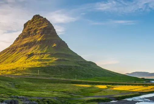 Scenic view of the Snæfellsnes Peninsula in Iceland with Kirkjufell mountain bathed in warm sunlight with lush green surroundings and the sea in the background.