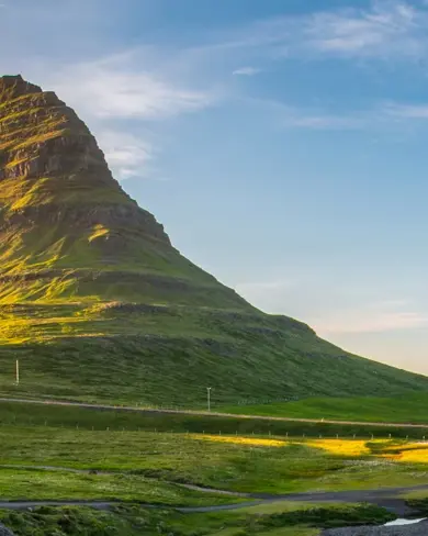 Scenic view of the Snæfellsnes Peninsula in Iceland with Kirkjufell mountain bathed in warm sunlight with lush green surroundings and the sea in the background.