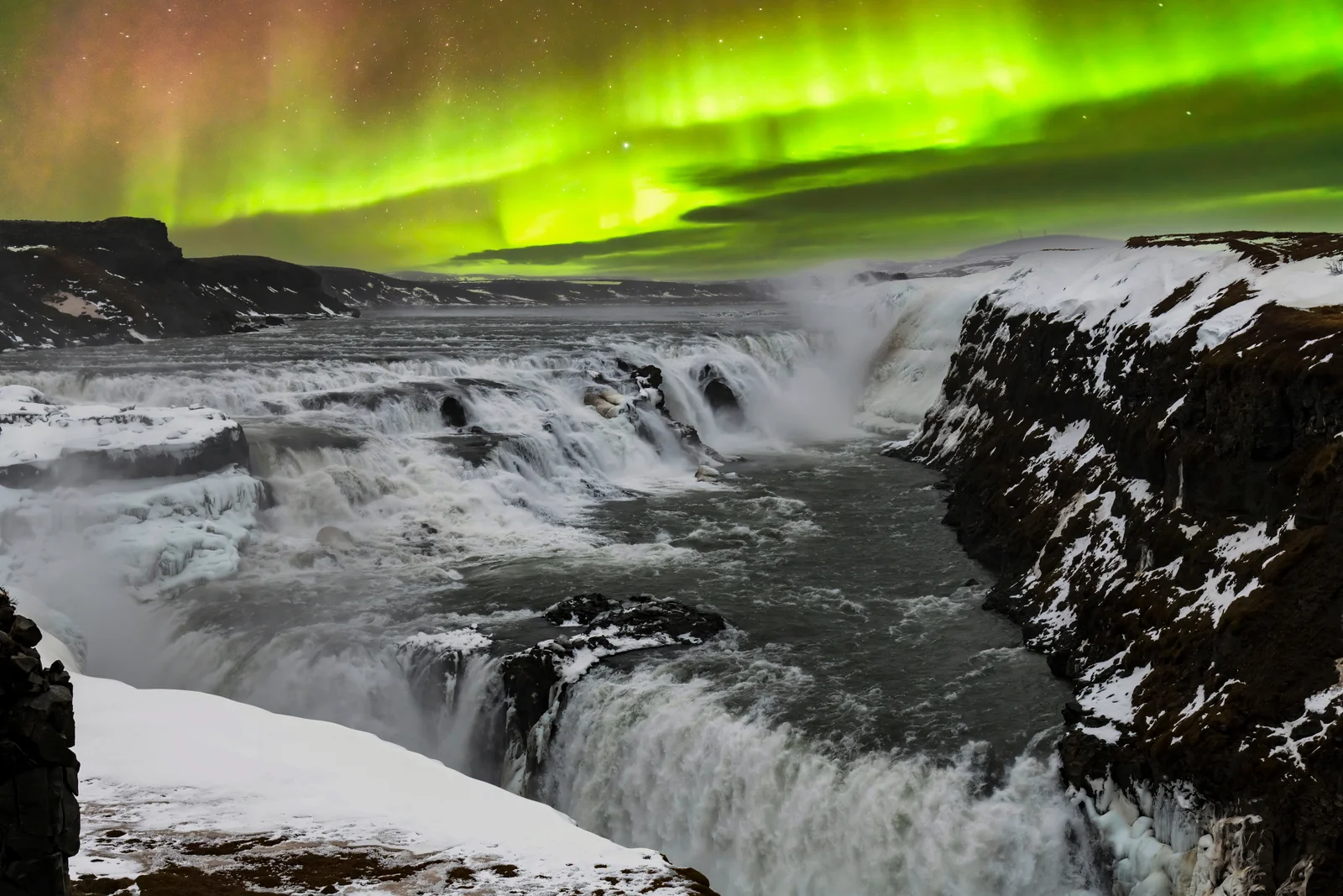 Panoramic scene of aurora borealis glowing above the icy Gullfoss waterfall in Iceland’s Golden Circle.