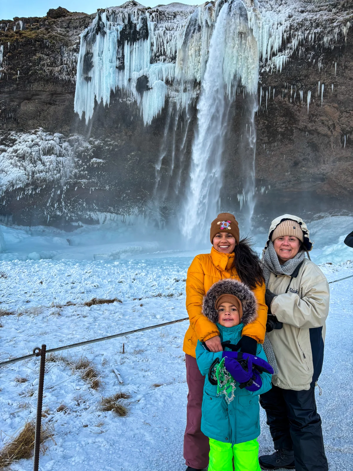 Family Of Travelers In Front Of Seljalandsfoss Waterfall, Visiting In Winter.