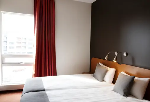 Bright double room with twin beds, large window, red curtains, and minimalistic Scandinavian design.