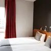 Bright double room with twin beds, large window, red curtains, and minimalistic Scandinavian design.