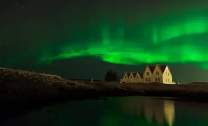 Northern lights dancing over a white house reflecting in a lake. 