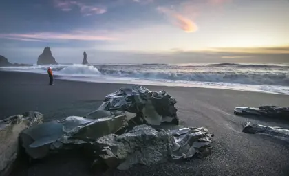 A stunning sunset at Reynisfjara Beach, Iceland, highlighting the towering basalt columns and the distant Reynisdrangar sea stacks against the backdrop of a dramatic sky.