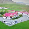 Aerial view of Gerði Guesthouse, a cozy farmstay with red rooftops, nestled in green fields near the coastline, featured on the Blue Ice Cave and Glacier Lagoon tour.