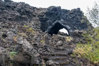 The church at Dimmuborgir lava field in Mývatn. A natural lava rock arch in Iceland, surrounded by rugged volcanic rocks and autumn foliage.