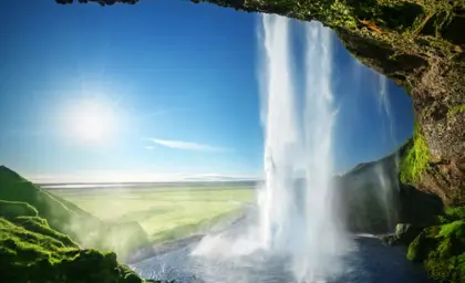 Seljalandsfoss waterfall in southern Iceland viewed from behind, with sunlight shining through the mist.