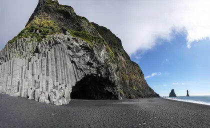 Basalt columns and cave at Reynisfjara black sand beach with Reynisdrangar sea stacks in the background, Iceland