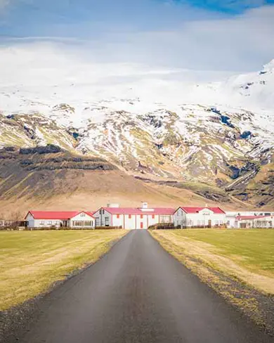 A scenic farm at the base of Eyjafjallajökull volcano in Iceland, surrounded by snow-covered mountains.