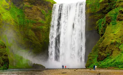 Skógafoss Waterfall cascading powerfully in Iceland, surrounded by lush green cliffs with tourists standing at its base.