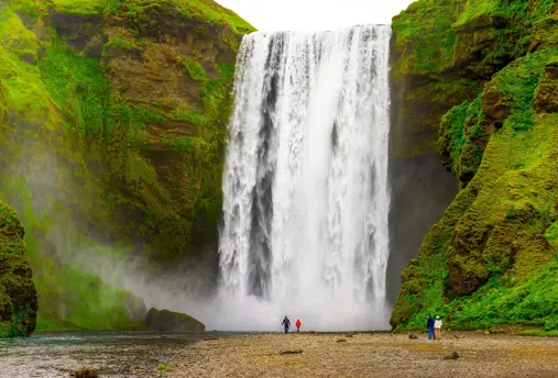 Skógafoss Waterfall cascading powerfully in Iceland, surrounded by lush green cliffs with tourists standing at its base.