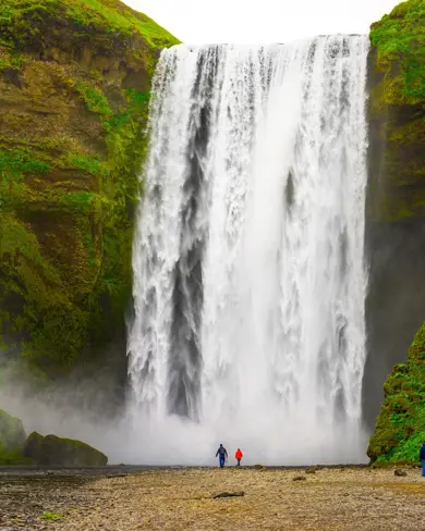 Skógafoss Waterfall cascading powerfully in Iceland, surrounded by lush green cliffs with tourists standing at its base.