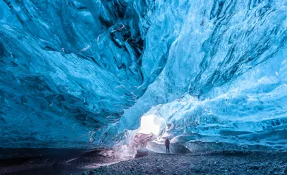 Traveler standing inside a vast and glowing blue ice cave in Vatnajökull glacier, surrounded by sculpted glacial walls on an unforgettable winter tour in Iceland.