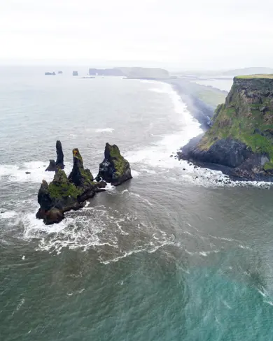 Aerial view of Reynisdrangar sea stacks along the rugged Icelandic coastline, captured from a tour highlighting the scenic beauty of the southern shores.