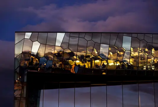 Evening view of La Primavera restaurant inside Harpa Concert Hall in Reykjavík, showcasing the iconic glass facade reflecting vibrant city lights and the night sky.
