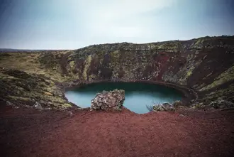 The vibrant red volcanic rock surrounding Kerid Crater Lake, Iceland.