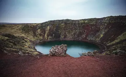 The vibrant red volcanic rock surrounding Kerid Crater Lake, Iceland.