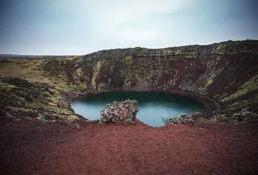 The vibrant red volcanic rock surrounding Kerid Crater Lake, Iceland.